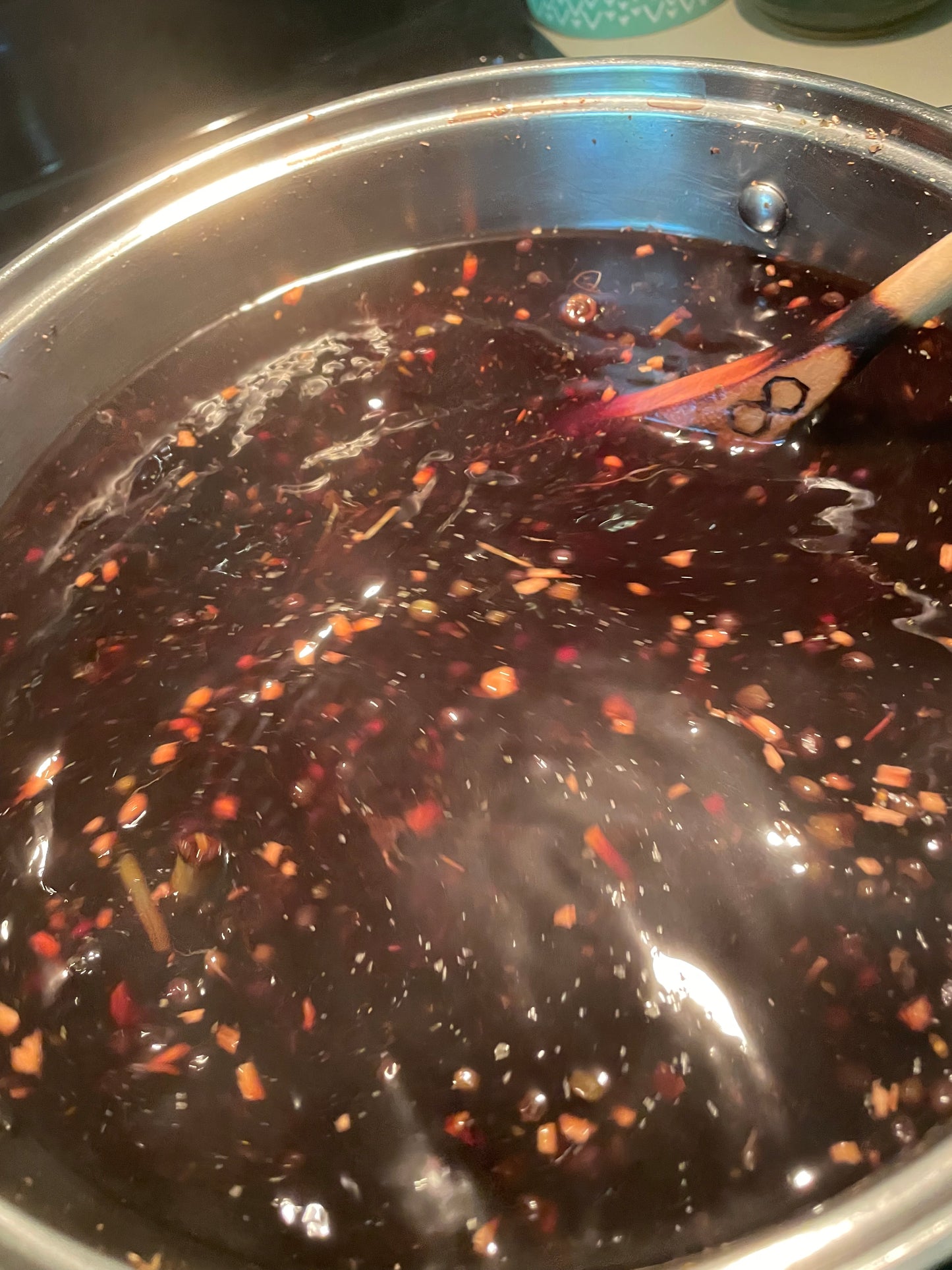 Chimney Sweep Tonic being prepared in a stainless steel pot on the stove, with a wooden spoon being used to stir. The spoon has an infinity symbol burn-carved on it.