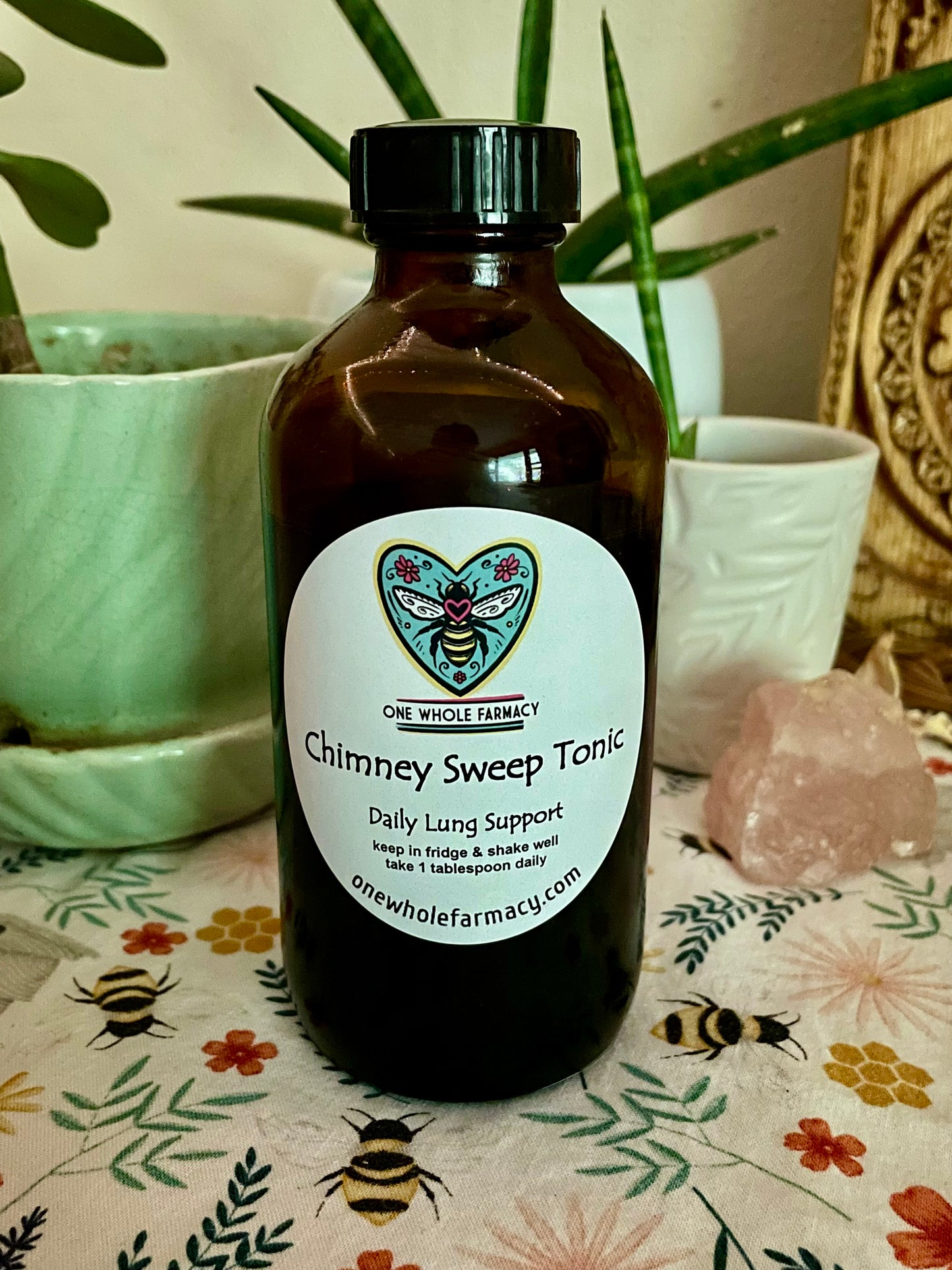 Bottle of 'Chimney Sweep Tonic' sitting on a table with plants and crystals